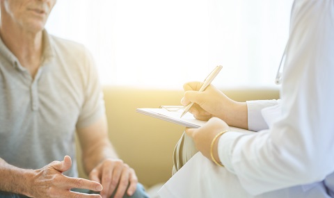 Faceless view of senior man talking to doctor in bright light while taking notes on clipboard